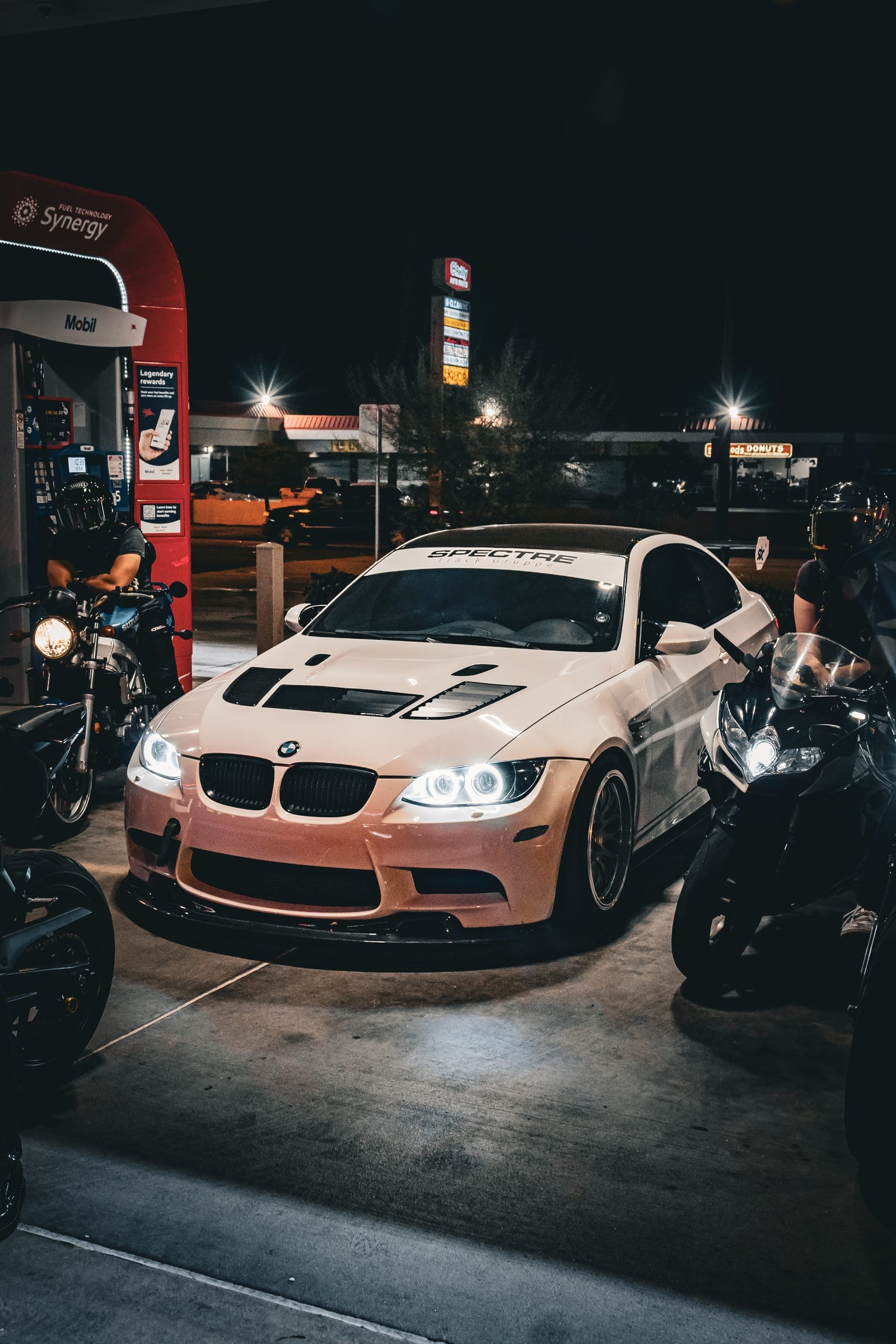 A white BMW and bikes parked at the pumps at night