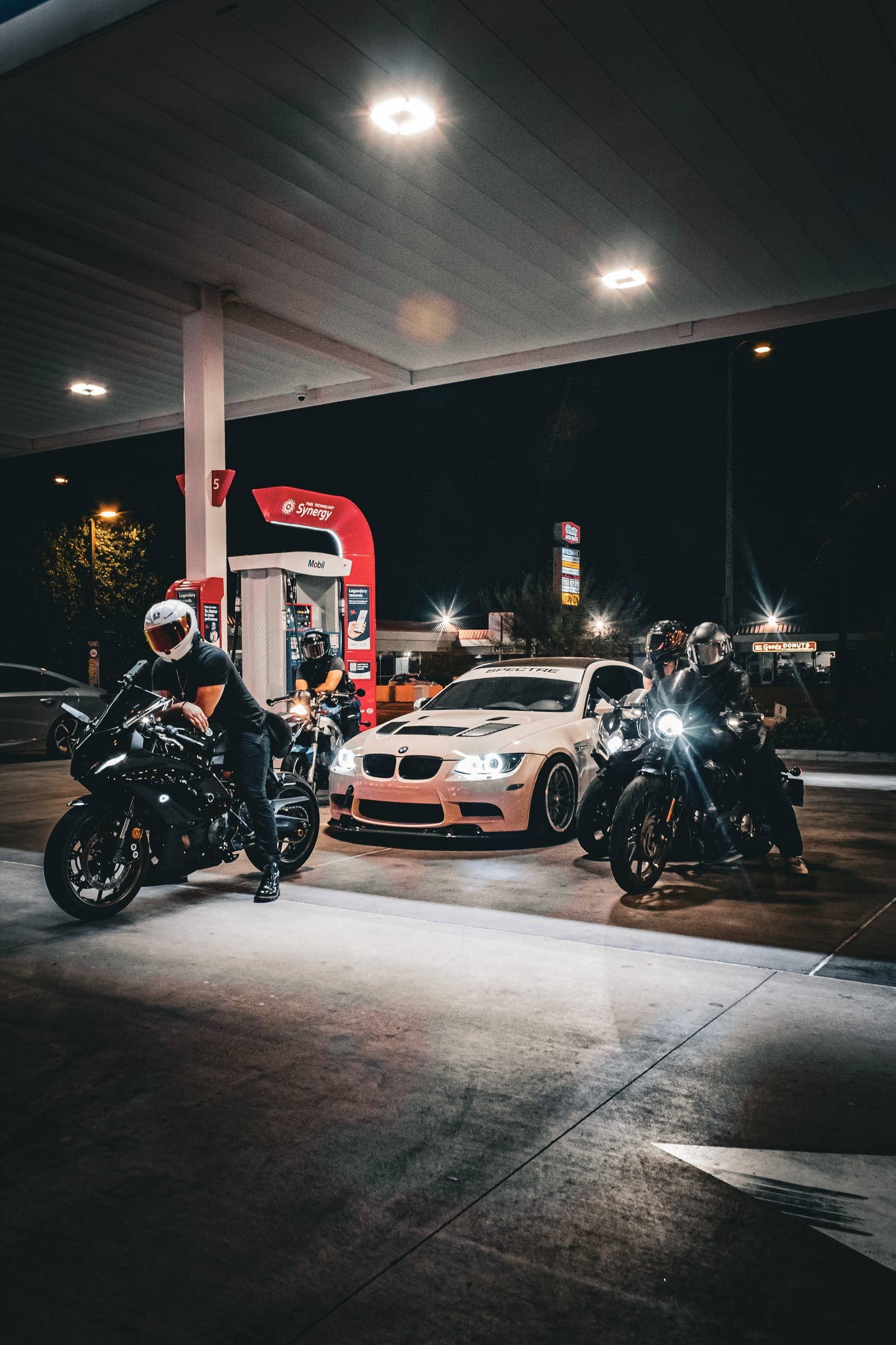 Riders and a white BMW under the canopy lights, seen wide
