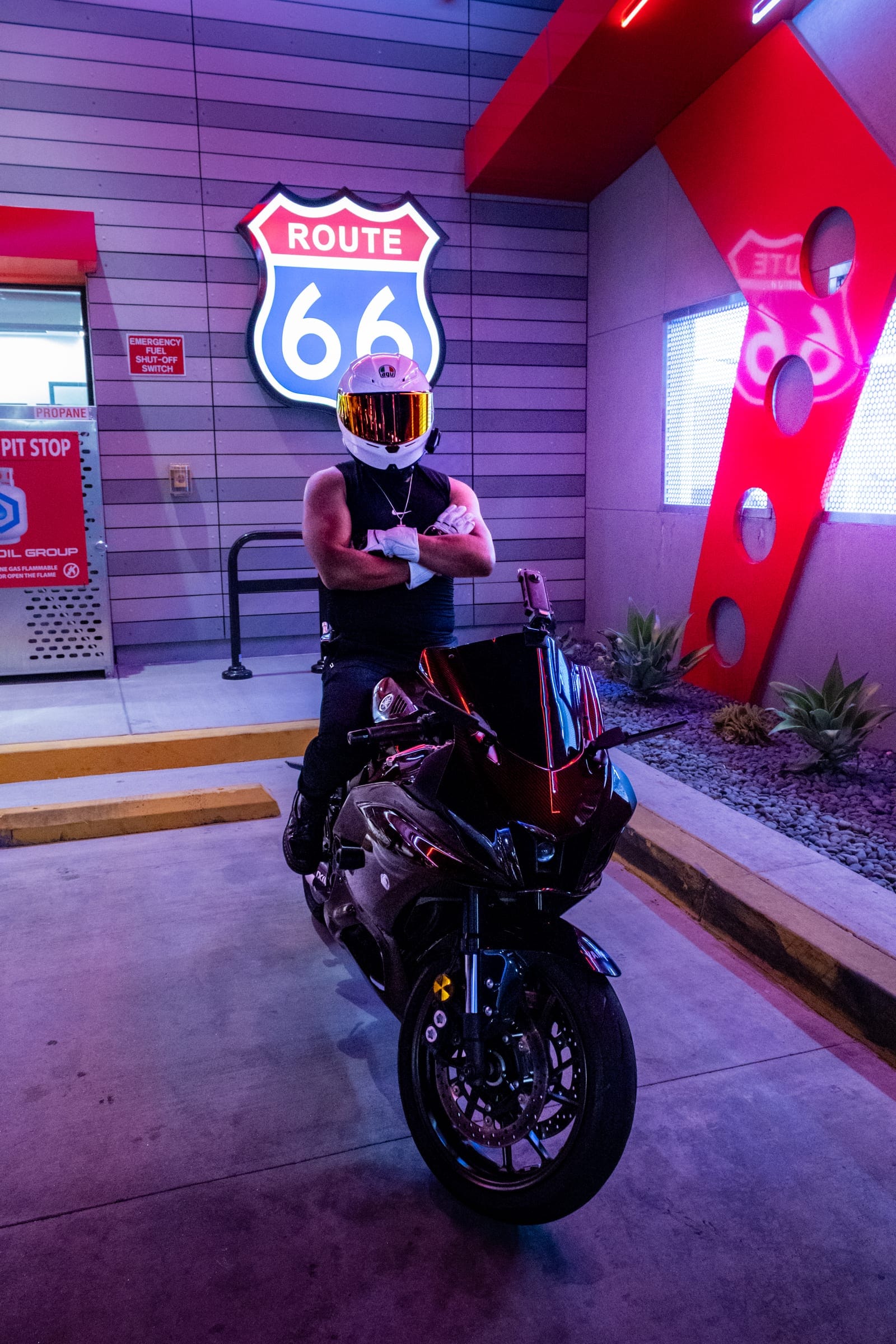 Rider in a white helmet, arms crossed, beside a dark sportbike