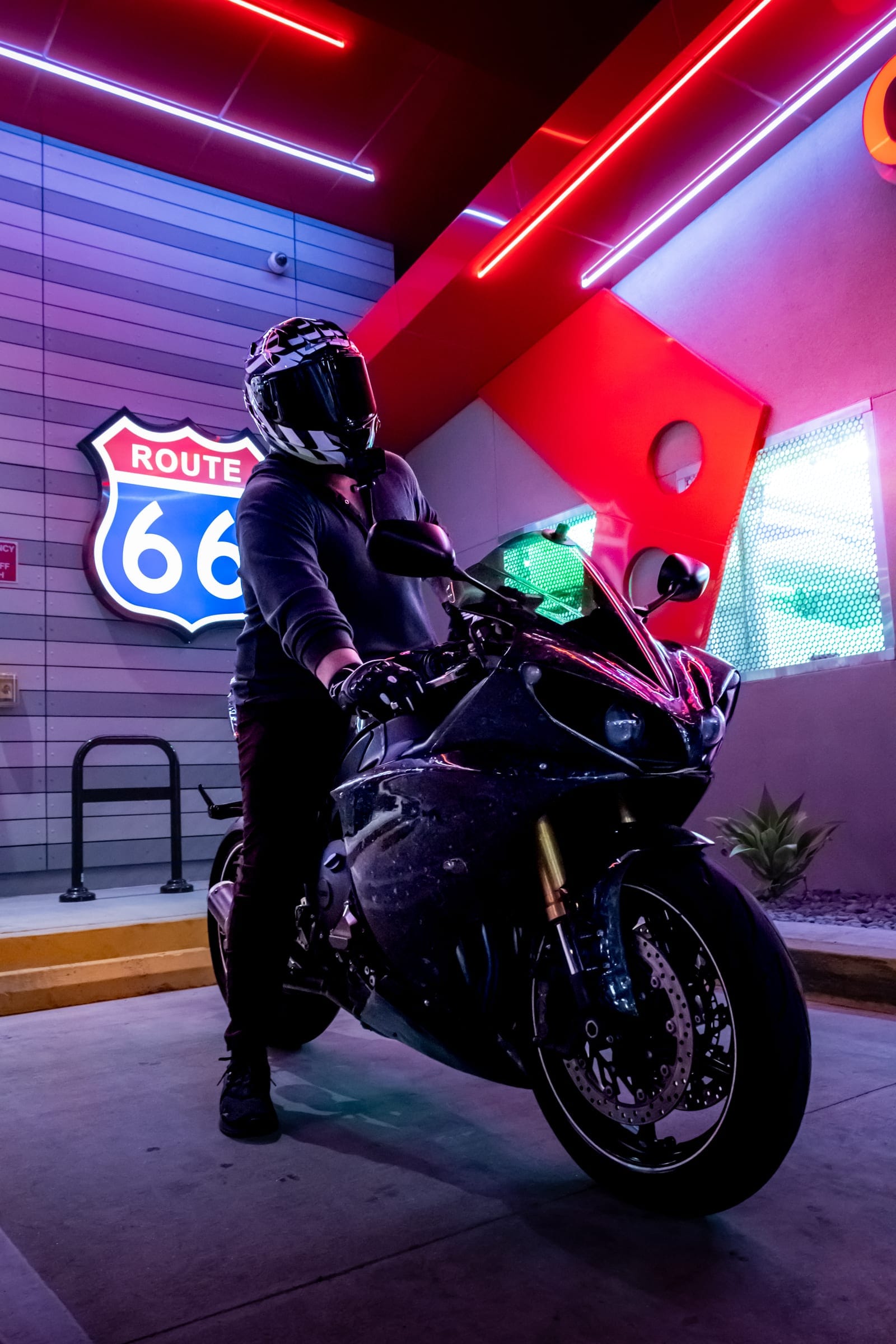 Rider on a black sportbike under red neon and the Route 66 sign