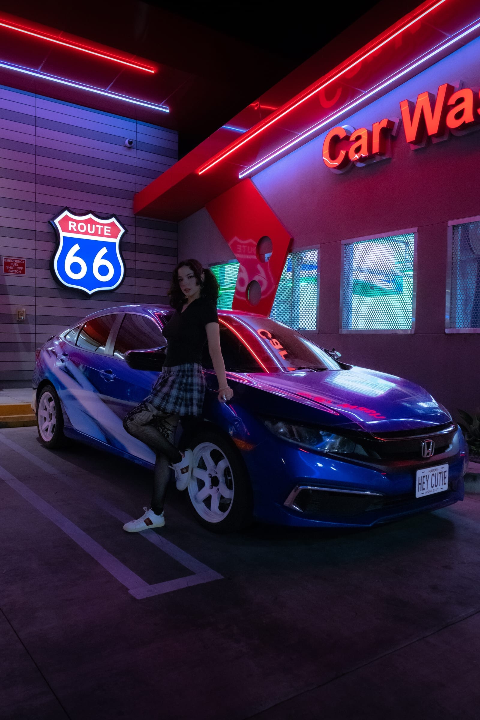 A blue Honda Civic under the Car Wash neon, its owner leaning on it
