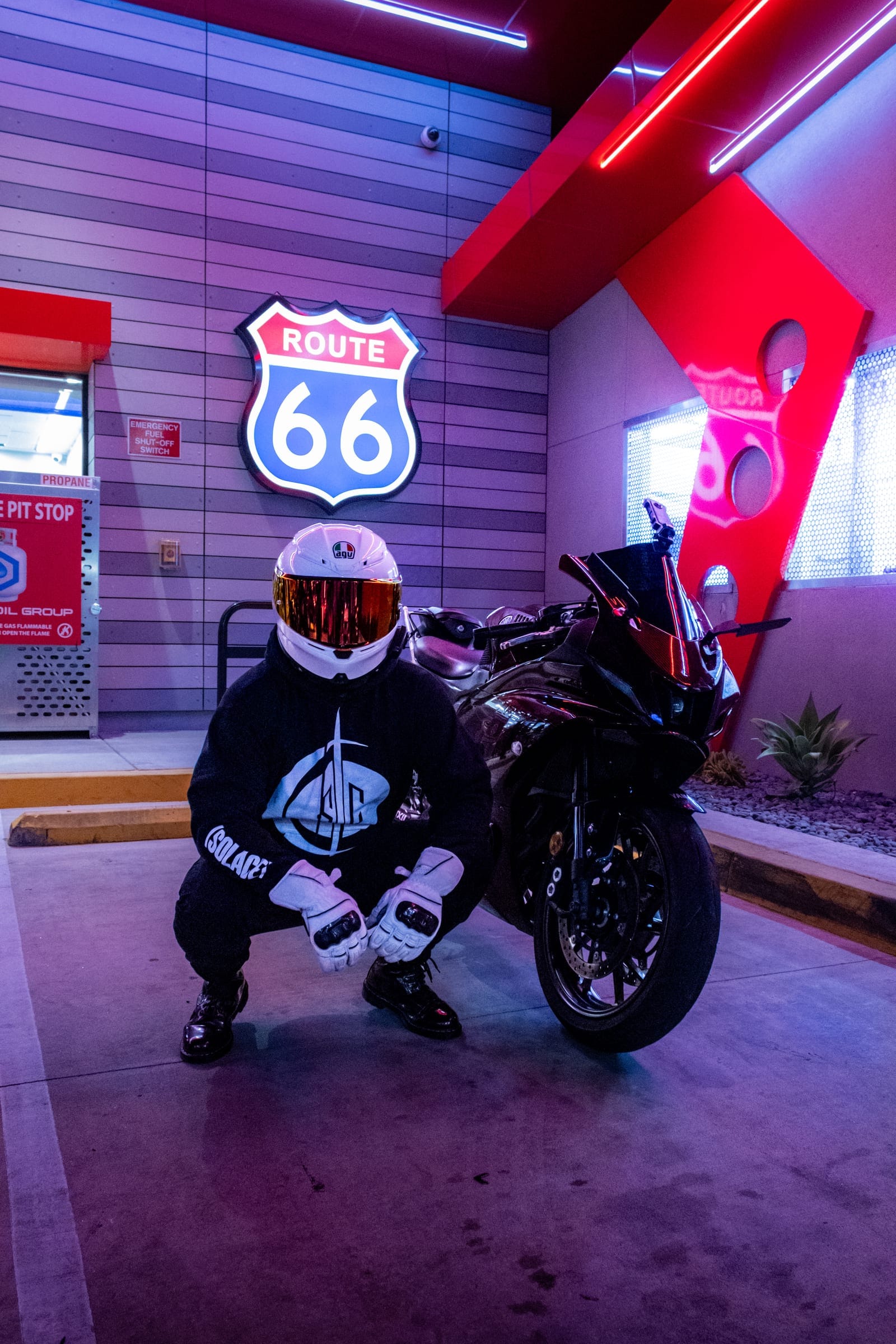 Rider in a white helmet and Solace hoodie crouched beside his sportbike
