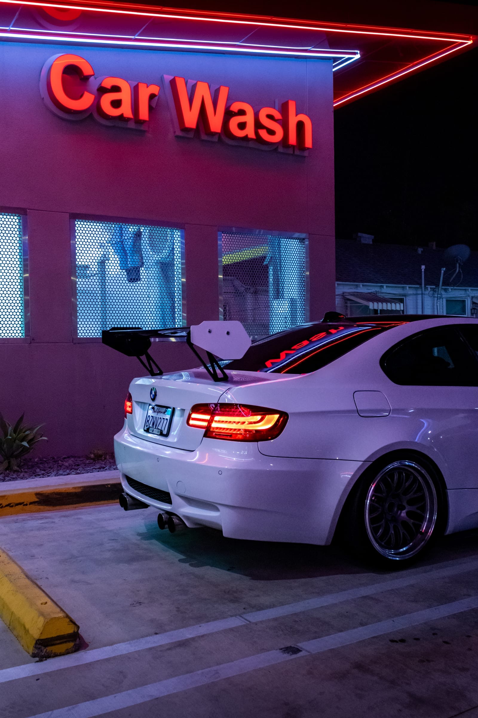 The white BMW M3 from behind, wing up, under the Car Wash sign